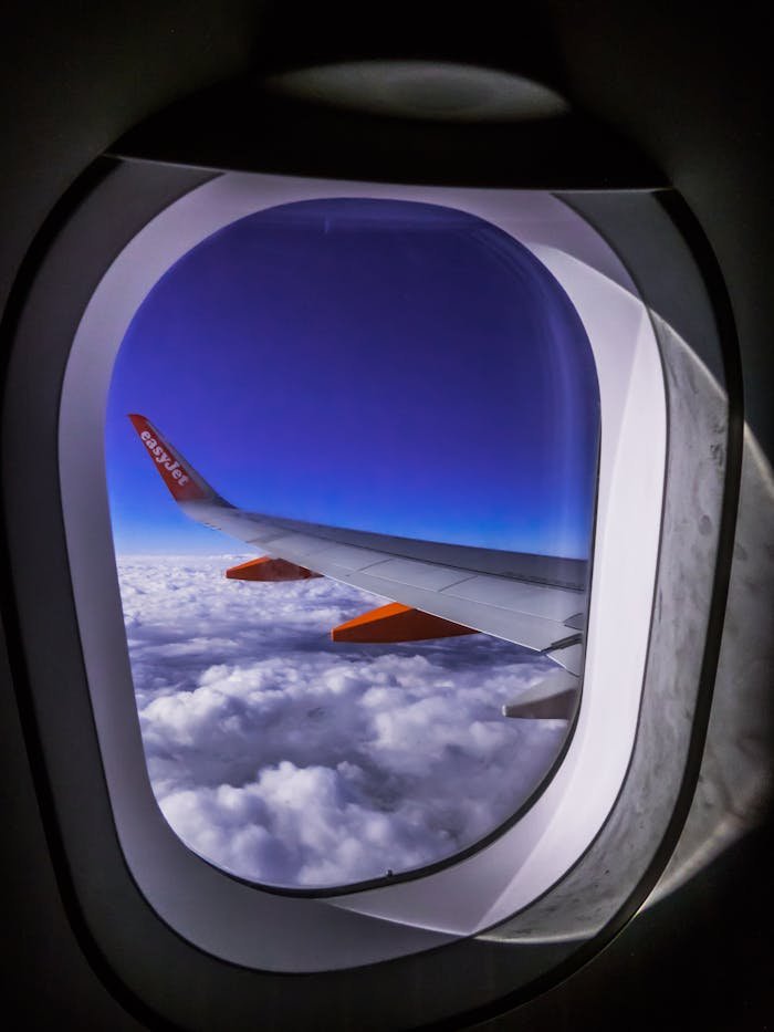 View of an airplane wing through the window with a vibrant blue sky and clouds below. Perfect for travel and aviation themes.